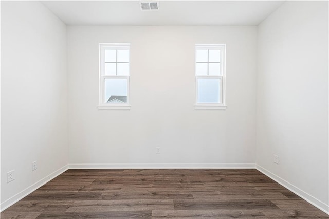 spare room featuring dark wood-type flooring, visible vents, and baseboards