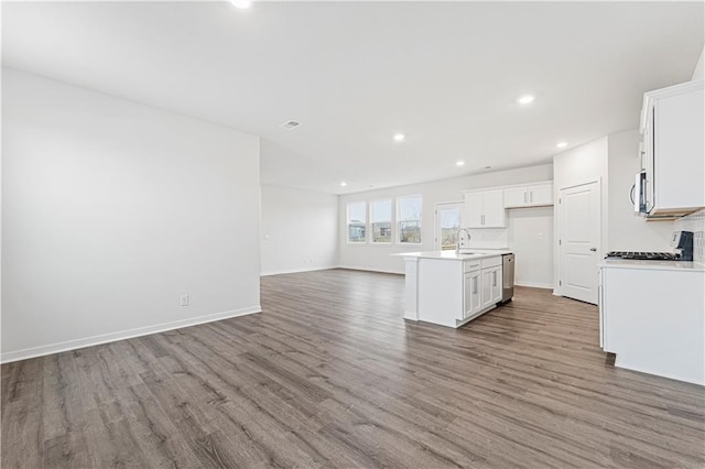 kitchen featuring a kitchen island with sink, a sink, white cabinetry, open floor plan, and light countertops