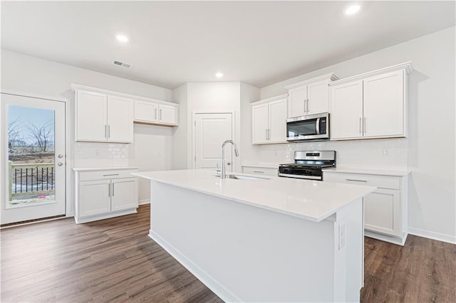 kitchen featuring dark wood-style flooring, light countertops, appliances with stainless steel finishes, white cabinets, and an island with sink