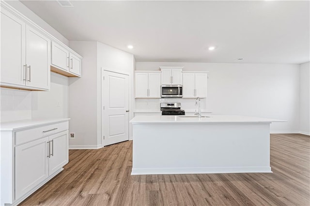 kitchen with stainless steel appliances, light countertops, a center island with sink, and white cabinetry