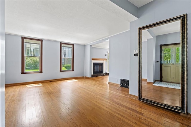 unfurnished living room featuring a textured ceiling, light hardwood / wood-style floors, and a tiled fireplace