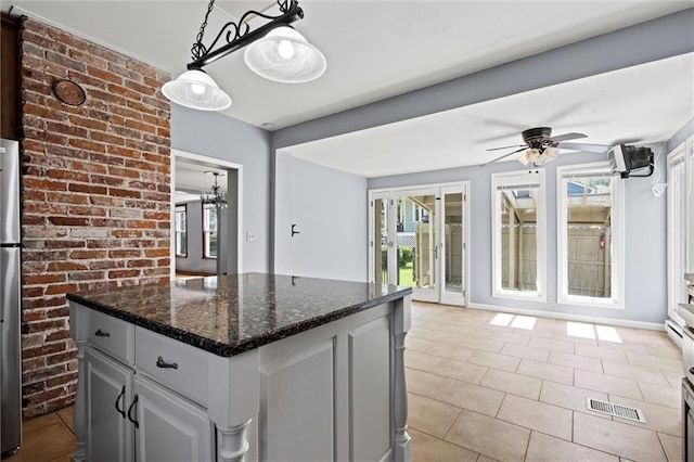 kitchen featuring dark stone counters, gray cabinetry, ceiling fan with notable chandelier, a kitchen island, and hanging light fixtures