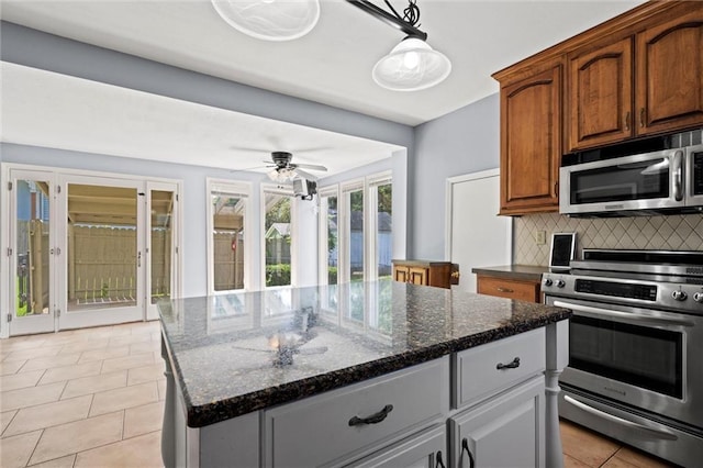 kitchen with gray cabinetry, a center island, dark stone countertops, tasteful backsplash, and stainless steel appliances