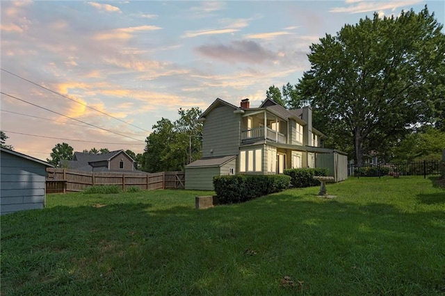 property exterior at dusk with a lawn, a balcony, and a shed