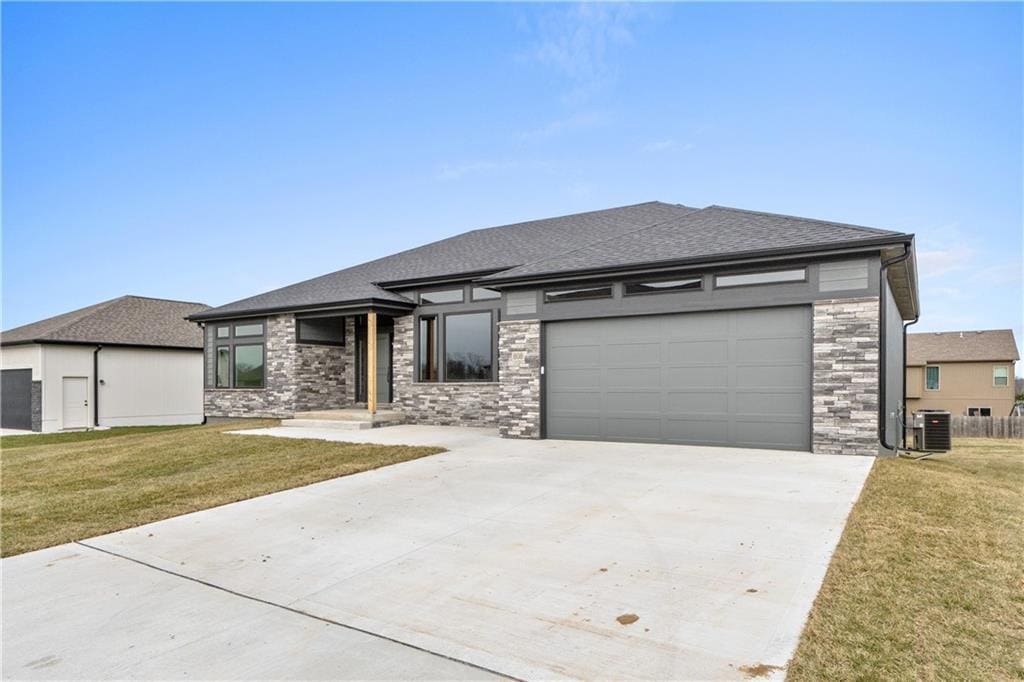 prairie-style house with concrete driveway, roof with shingles, an attached garage, cooling unit, and a front yard