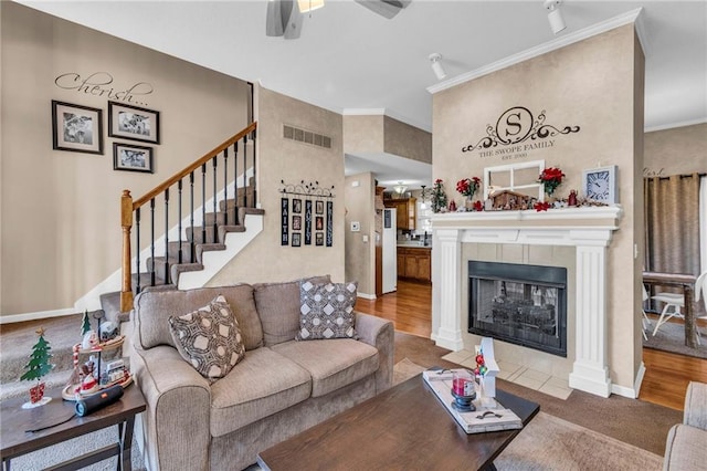 living room with a tiled fireplace, crown molding, hardwood / wood-style floors, and ceiling fan