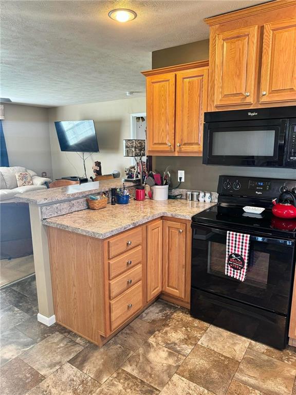 kitchen with kitchen peninsula, light stone counters, black appliances, and a textured ceiling