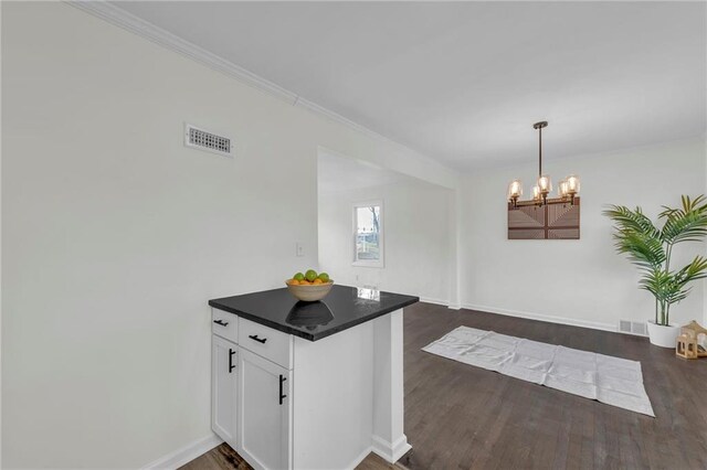 kitchen featuring dark hardwood / wood-style flooring, crown molding, pendant lighting, an inviting chandelier, and white cabinetry