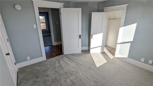 unfurnished bedroom with a walk in closet, a closet, and dark colored carpet