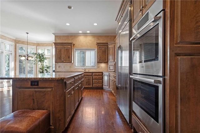 kitchen with appliances with stainless steel finishes, hanging light fixtures, a kitchen island, dark hardwood / wood-style flooring, and decorative backsplash