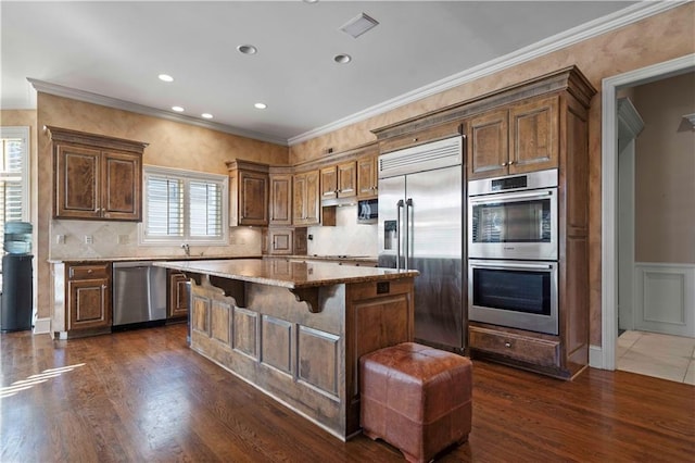 kitchen with a breakfast bar, light stone counters, crown molding, appliances with stainless steel finishes, and a kitchen island