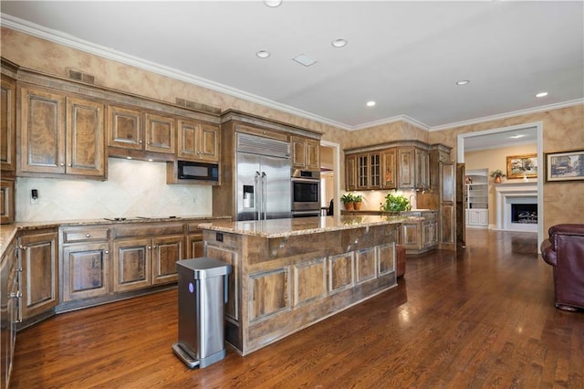 kitchen with a kitchen island, dark hardwood / wood-style flooring, light stone counters, stainless steel appliances, and crown molding