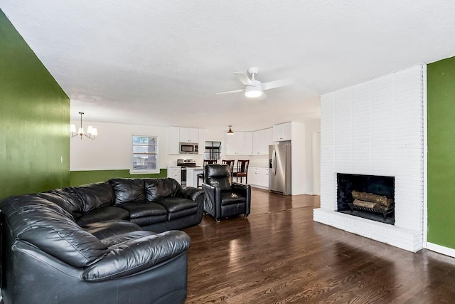 living room featuring ceiling fan with notable chandelier, dark hardwood / wood-style floors, and a brick fireplace