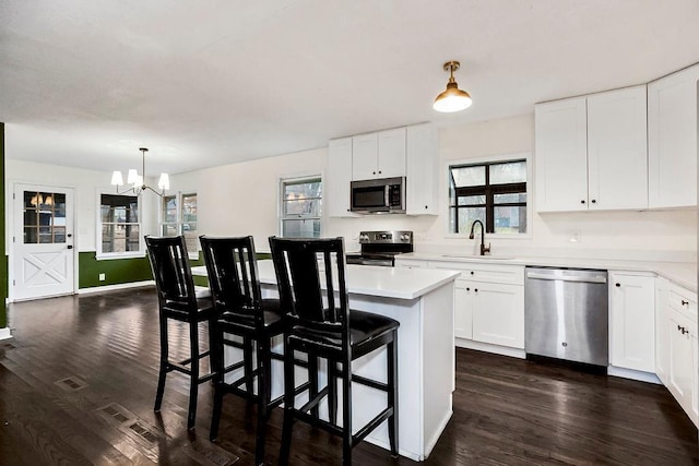 kitchen featuring appliances with stainless steel finishes, decorative light fixtures, white cabinetry, and a kitchen island