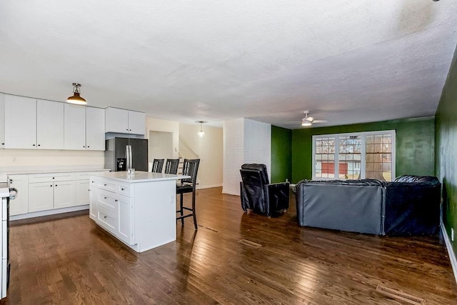 kitchen with stainless steel fridge, dark hardwood / wood-style flooring, a breakfast bar, white cabinets, and an island with sink