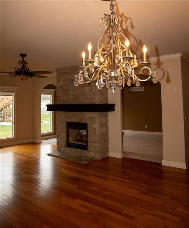 unfurnished living room with ceiling fan, a stone fireplace, wood-type flooring, and ornamental molding