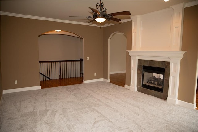 unfurnished living room featuring a tile fireplace, crown molding, ceiling fan, and light carpet