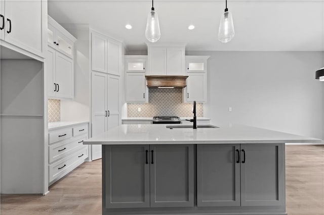 kitchen featuring sink, hanging light fixtures, an island with sink, and white cabinets