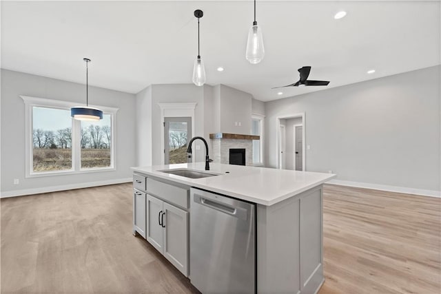 kitchen featuring pendant lighting, an island with sink, sink, stainless steel dishwasher, and light hardwood / wood-style floors