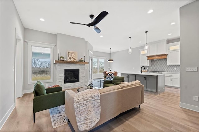 living room featuring sink, a fireplace, ceiling fan, and light wood-type flooring