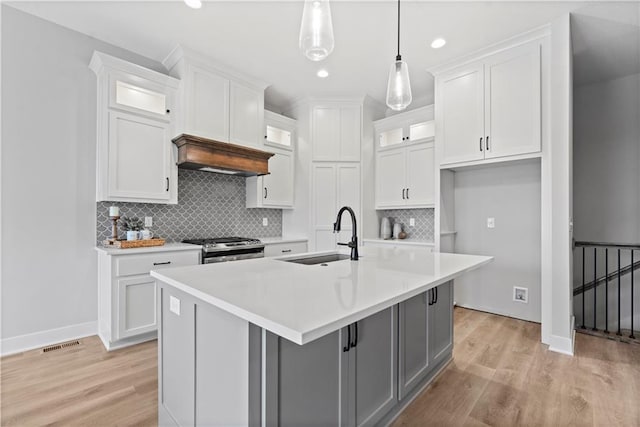 kitchen featuring sink, gas range, pendant lighting, a kitchen island with sink, and white cabinets