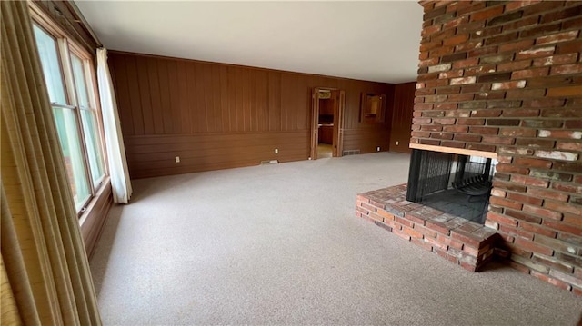 unfurnished living room with a brick fireplace, light colored carpet, and wood walls