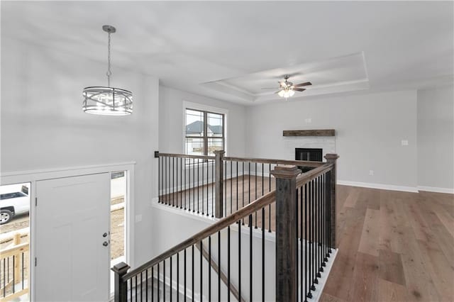 corridor with a tray ceiling, an inviting chandelier, and hardwood / wood-style flooring