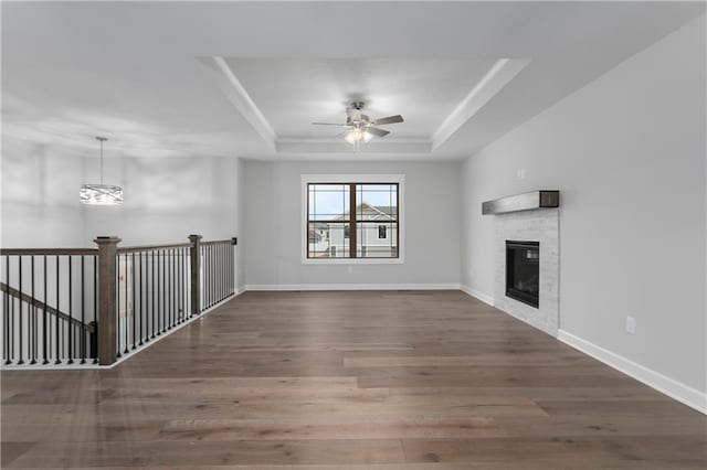 unfurnished living room featuring a raised ceiling, ceiling fan with notable chandelier, and dark hardwood / wood-style flooring