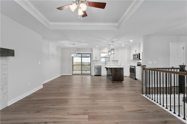 unfurnished living room with sink, dark hardwood / wood-style floors, ceiling fan, ornamental molding, and a tray ceiling