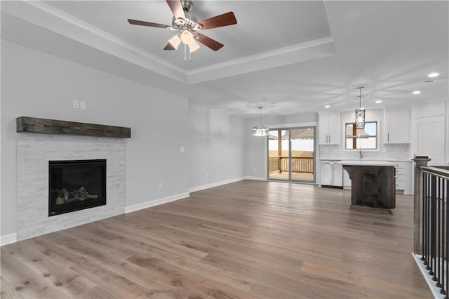 unfurnished living room with a tray ceiling, ceiling fan, sink, light hardwood / wood-style flooring, and a tiled fireplace