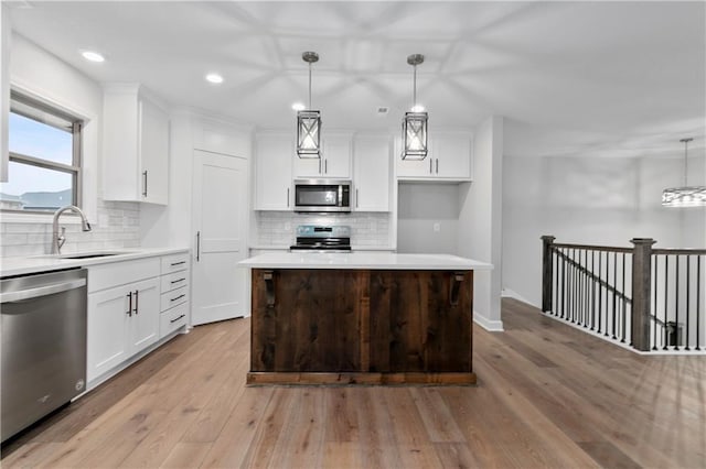 kitchen featuring sink, light hardwood / wood-style floors, decorative light fixtures, a kitchen island, and appliances with stainless steel finishes