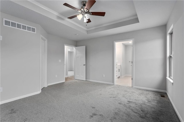 unfurnished bedroom with a raised ceiling, ensuite bath, ceiling fan, and carpet