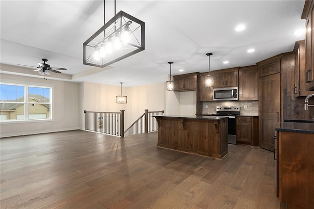 1316 N Holland Ct, Independence, MO 64056 - kitchen with appliances with stainless steel finishes, tasteful backsplash, dark wood finished floors, dark countertops, and a kitchen island