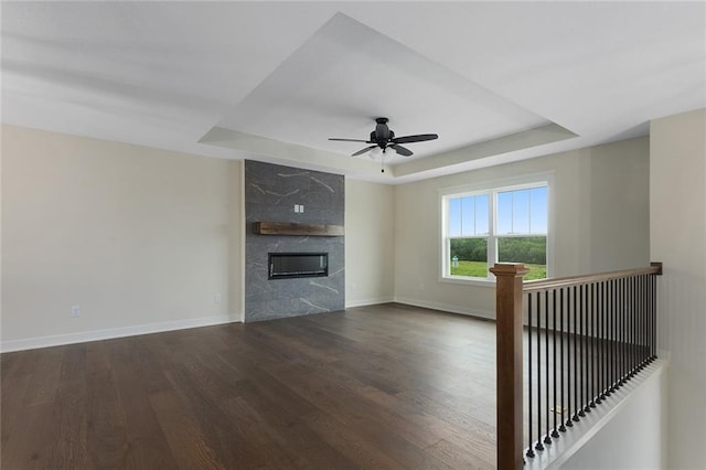 1316 N Holland Ct, Independence, MO 64056 - unfurnished living room with a raised ceiling, dark wood-style floors, a ceiling fan, baseboards, and a high end fireplace