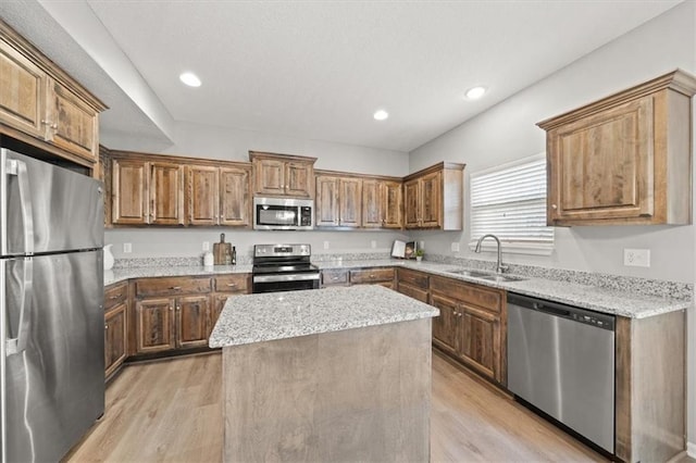 kitchen featuring sink, stainless steel appliances, light stone counters, a kitchen island, and light wood-type flooring