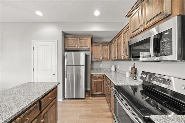 kitchen with light wood-type flooring, stainless steel appliances, and light stone counters