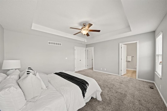 carpeted bedroom with ceiling fan, a raised ceiling, and connected bathroom