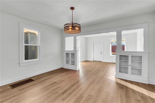 interior space with light hardwood / wood-style floors, decorative columns, and a notable chandelier