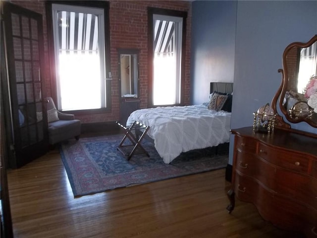 bedroom featuring multiple windows, brick wall, and hardwood / wood-style floors