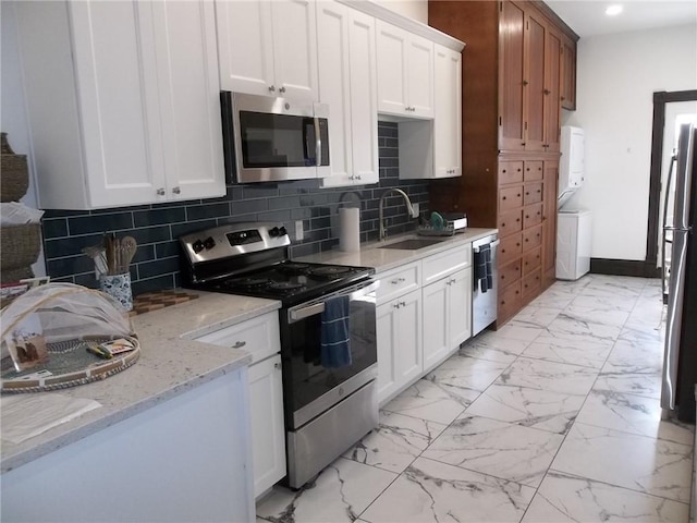 kitchen featuring sink, white cabinetry, stainless steel appliances, stacked washer and clothes dryer, and light stone countertops