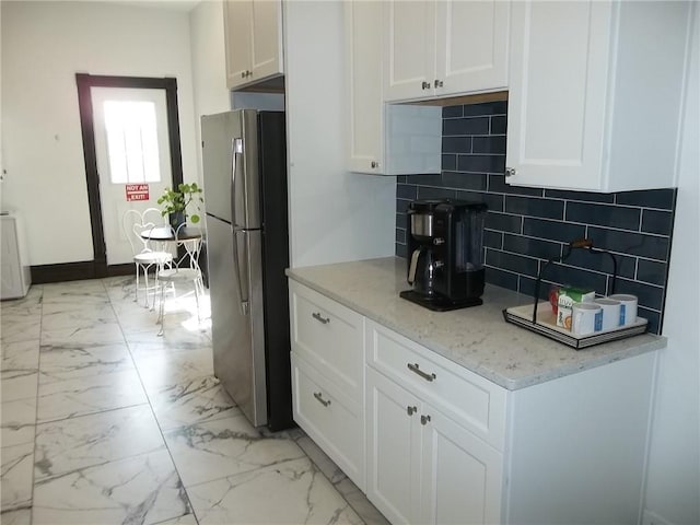 kitchen featuring stainless steel refrigerator, white cabinetry, light stone countertops, and decorative backsplash