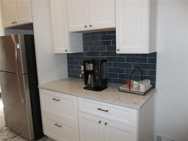 kitchen with white cabinetry, light stone countertops, backsplash, and stainless steel refrigerator