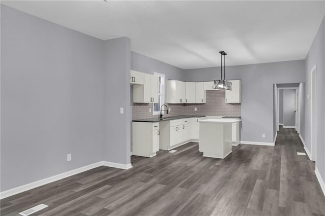 kitchen with sink, dark wood-type flooring, a kitchen island, decorative light fixtures, and white cabinets