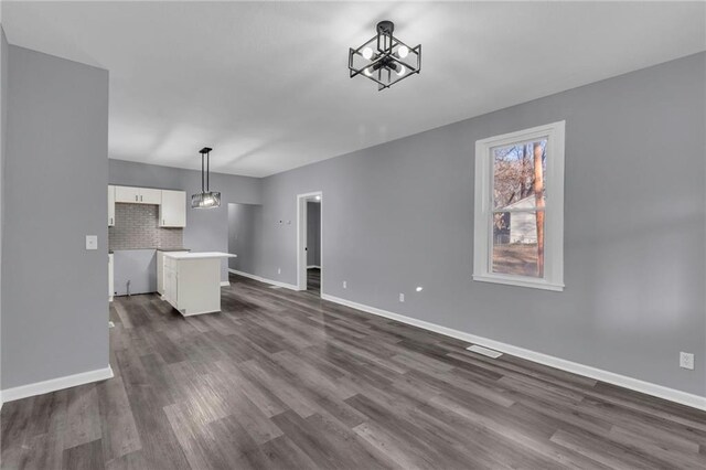 unfurnished living room with a chandelier and dark wood-type flooring