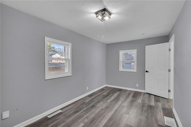 empty room with hardwood / wood-style floors, a textured ceiling, and a wealth of natural light