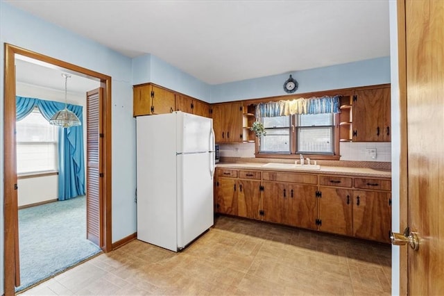 kitchen with sink, white refrigerator, tasteful backsplash, light carpet, and decorative light fixtures