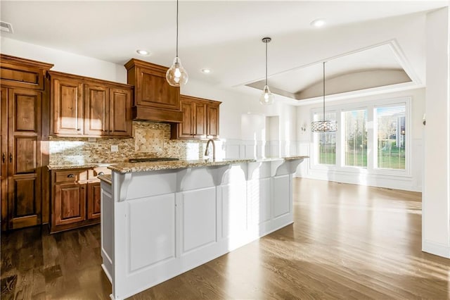 kitchen with pendant lighting, dark hardwood / wood-style floors, light stone countertops, and an island with sink