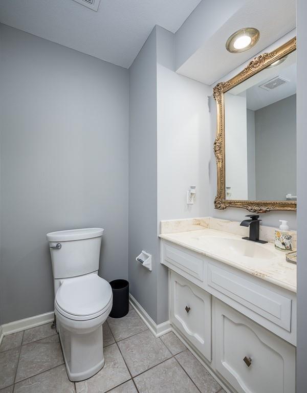 half bathroom with tile patterned flooring, visible vents, baseboards, toilet, and vanity