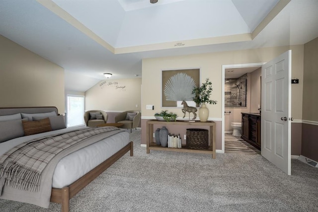 carpeted bedroom featuring a raised ceiling, vaulted ceiling, baseboards, and ensuite bathroom