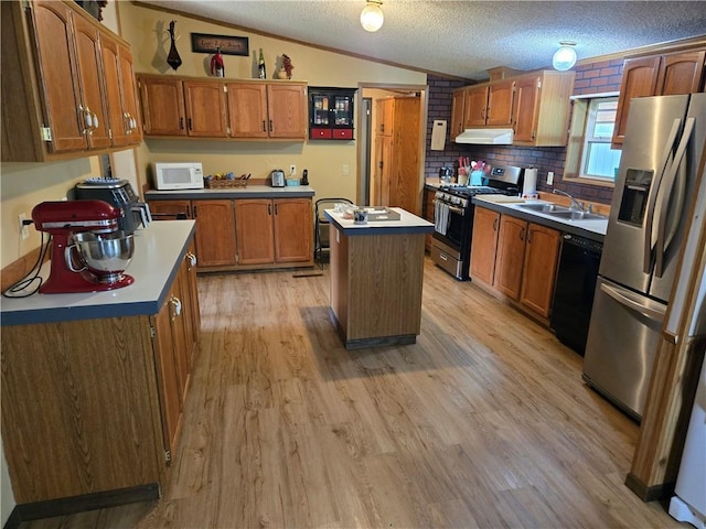 423 Elm St, Mound City, KS 66056 - kitchen featuring appliances with stainless steel finishes, under cabinet range hood, a kitchen island, brown cabinetry, and vaulted ceiling